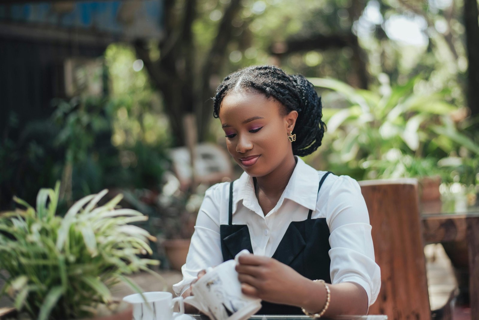 A young woman sipping coffee in an outdoor garden, surrounded by greenery and natural light.