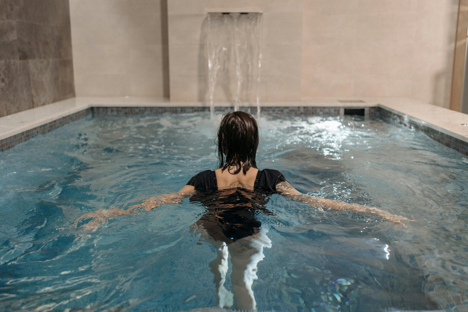 A woman enjoying a swim in an indoor pool with a waterfall feature.