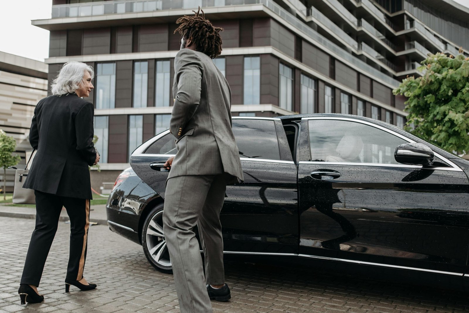 Business professionals exiting luxury car near modern building in city setting.